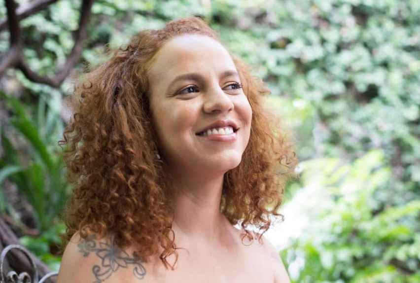 Letícia sorrindo, com cachos acobreados abaixo do ombro