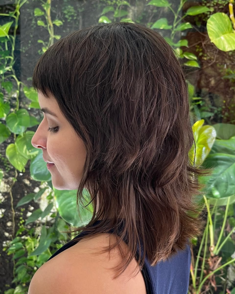 Juliana de perfil no jardim, com franja curta e cabelo em camadas na altura dos ombros