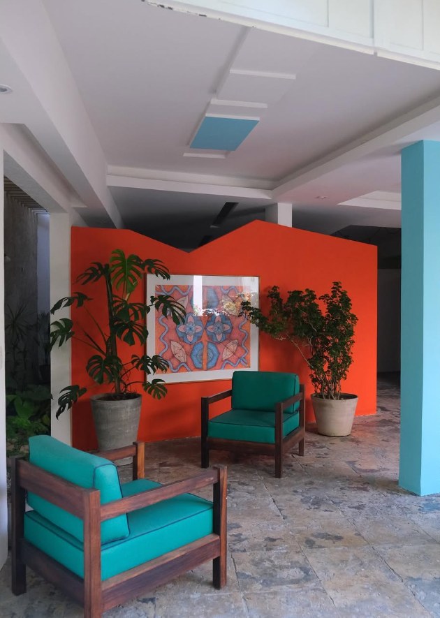 Sala de espera com parede laranja, quadro e poltronas turquesa